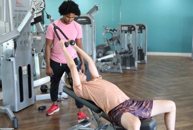 Personal trainer assisting a client with strength training in a gym